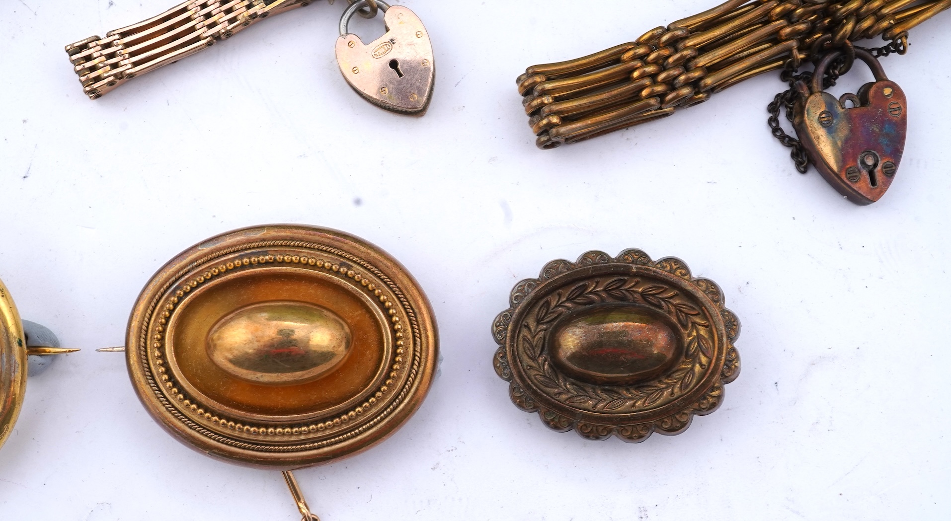 A group of gilt metal/pinchbeck jewels, 19th and early 20th century, comprising: a brooch of knotted design; two gate bracelets; a fancy link bracelet; an open-faced pocket watch; two oval panel brooches, and two watch c